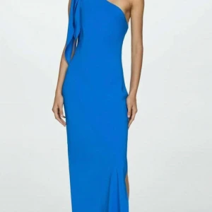 Blå långklänning med oneshoulder - Snygg blå långklänning med oneshoulder och slits på sidan. Klänningen har en cool asymmetrisk design med ett band som hänger ner från axeln. Perfekt för dig som vill sticka ut med en stilren och modern look. 
