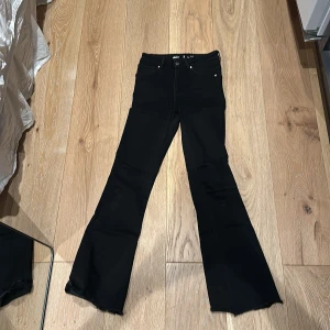 Svarta bootcut jeans från Never Denim - Säljer ett par svarta bootcut jeans från Never Denim i storlek S. Byxorna har klassisk femficksdesign, rå kant vid benslut och är tillverkade av bomull och polyester med lite elastan för stretch. 