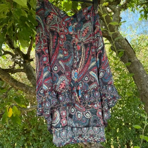 Mönstrad kjol med knappar - Säljer en färgstark kjol med paisley- och blommönster i blått, rött, beige och svart. Kjolen har volangdetaljer och knappar framtill. Materialet är lätt och luftigt, perfekt för varma dagar. Unik boho-vibe och snygg passform. Storlek 3 som enligt deras storleksguide motsvarar en storlek L.  Mycket fint skick, jag hittar inga synliga anmärkningar eller defekter.