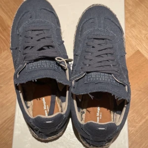 Maison Margiela blå sneakers  - Unika sneakers från Maison Margiela i ljusblå canvas med råa kanter och snörning. Sulan är i flätad jute som ger en espadrille-vibe och insidan har bruna läderdetaljer. Perfekt för dig som gillar statement och cool design.
