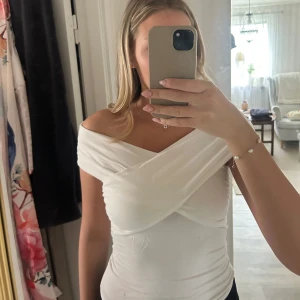 Vit topp från Gina  - Säljer en vit omlott topp från Gina Tricot i storlek S. Toppen har offshoulder-design med breda omlottband över bysten och är figurnära. Materialet är mjukt och stretchigt, perfekt för en snygg och trendig look. Passar dig som gillar stilrena och moderna plagg.