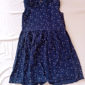 Blå blommig klänning från H&M - Supersöt blå klänning från H&M i ekologisk bomull. Den är ärmlös och har ett vitt blommigt mönster över hela klänningen. Kjolen är lätt utställd och midjan markerad, perfekt för dig som gillar en enkel men gullig stil. Säljs pga flytt.