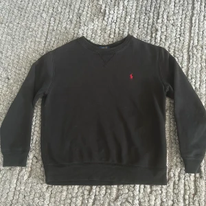 Svart sweatshirt från Polo Ralph Lauren - Svart sweatshirt från Polo Ralph Lauren. Riktigt snygg passar de mesta med klassisk röd polo Ralph lauren logga. Passar mellan 155-165cm lång och ett litet hål som inte är synligt annars bra passform och bra skick