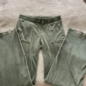 Gröna Juicy Couture byxor - Snygga gröna byxor från Juicy Couture i storlek S. Byxorna har bred resår i midjan med snörning, stora fickor fram och bak med knappdetaljer. Mjukt material som känns skönt mot huden, perfekt för chill eller häng med kompisar.
