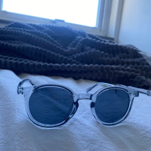 Runda solglasögon med transparent båge - Snygga solglasögon med rund form och transparent plastbåge. Glasen är mörka och ger en cool kontrast mot den klara ramen. Perfekta för dig som vill ha en stilren och modern look i sommar.
