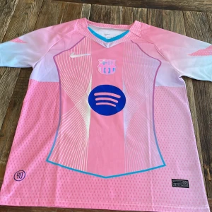 Barça Bonmatí #14 rosa Nike tröja - Säljer en officiell FC Barcelona Bonmatí #14 matchtröja från Nike i rosa och vitt med blå detaljer. Tröjan har korta ärmar, V-ringad krage med turkos kant, tryckt Spotify-logga och klubbmärke på bröstet. Materialet är lätt och ventilerande Dri-FIT polyester. Pris kan diskuteras!