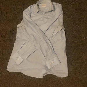 Ljusblå skjorta från Jack & Jones - Snygg ljusblå skjorta från Jack & Jones i storlek M. Klassisk modell med krage, långa ärmar och knappar framtill. Tillverkad i mjuk bomull som känns skön mot huden. Perfekt för dig som gillar stilrena och enkla plagg. 