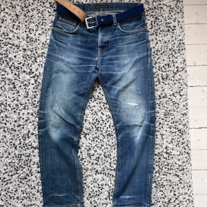 Blå jeans från Nudie Jeans Co W32 - Säljer ett par snygga blå jeans från Nudie Jeans Co i storlek W32 L32 . Sleepy Sixten modell. Går inte att få tag på längre då de ej tillverkas något mer, sjukt snygg tvätt.  Jeansen har klassisk femficksdesign, slitningar och lagad patch på ena knät, samt coola broderade detaljer på bakfickorna. Materialet är robust denim och passformen är rak med normal midja.