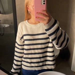Randig stickad tröja från Lindex - Säljer en ribbstickad tröja från Lindex i storlek 158/164. Tröjan är vit med svarta ränder. Den har ett litet hål vid vristen men det kan sys enkelt 