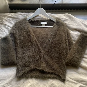 Brun fluffig kofta från Monki💗💗 - Supermjuk och fluffig brun kofta från Monki i storlek S. Koftan har v-ringning, tre knappar framtill och långärmade ärmar. Den är croppad och har en riktigt cozy vibe, perfekt för kyliga dagar. Materialet är pälsliknande syntet som känns lyxigt och skönt mot huden.