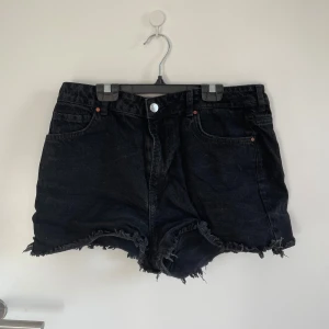 Svarta jeansshorts med fransad kant - Svarta jeansshorts från bikbok i storlek L med midwaist passform. De har klassiska fem fickor, knapp och dragkedja framtill samt rå, fransad kant nedtill. 