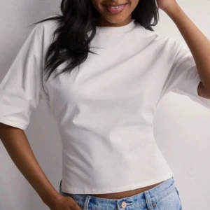 Vit topp med knyt i ryggen - Säljer en vit croppad topp med korta ärmar och snygg öppen rygg med knytband. T-shirten har en clean och enkel look framtill, medan ryggen har en cool twist med knyt som gör den extra trendig. Perfekt till jeans eller kjol för en chill vibe.