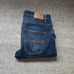 Blå Nudie Jeans Grim Tim - Säljer ett par klassiska blå jeans från Nudie Jeans. Jeansen är nästan helt oanvända i nyskick. Köpta från deras egna affär på söder. Perfekt för dig som vill ha en tidslös och klassisk look! Nypris 1600, pris kan diskuteras vid snabb affär!