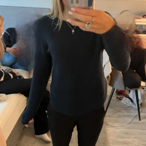 Mörkblå stickad tröja med slits - Säljer en mörkblå stickad tröja med lång ärm och rund hals. Tröjan har en snygg slits på sidan som ger en cool detalj. Perfekt att matcha med svarta jeans eller kostymbyxor. Enkel och stilren design som funkar till många olika looks.