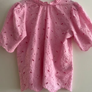 Rosa blus med broderade detaljer - Söt rosa blus med broderade blommor och hålmönster. Blusen har korta puffärmar och vågig kant nedtill. Märket är Lindex!💕köparen står för frakt! 