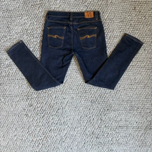 Mörkblå jeans från Nudie Jeans Co - Snygga mörkblå jeans från Nudie Jeans Co i klassisk femficksmodell med kontrastfärgade sömmar och logga på bakfickan. Modellen har smal passform och raka ben, tillverkade i slitstarkt bomullsjeansmaterial. Perfekt för dig som gillar stilrena och tidlösa jeans.
