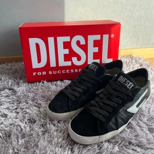 Svarta och vita sneakers från Diesel - Säljer ett par snygga Diesel sneakers i svart och vitt skinn med coola detaljer och röd undersida. Liten fläck på ena skon. Boxen medföljer.