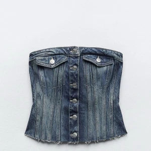 Jeans korsett tubtopp med knappar - Cool tubtopp i jeansmaterial med korsettform och snygga silverknappar framtill. Toppen har två fickor med lock och rå kant nedtill för en edgy vibe. Perfekt för dig som vill sticka ut med en unik denimlook.