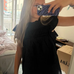 Svart blus med volangärmar - Säljer en svart blus med korta volangärmar och diskret prickigt mönster. 