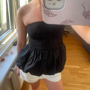 Svart bandeau tubtopp med volang - Säljer en svart bandeau tubtopp med volang nedtill. Toppen är axelbandslös och har en tight passform upptill med en puffig, volangig nederdel. Storlek S och nästan oanvänd