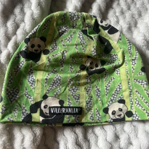 Grön panda-mössa från Villervalla - Säljer en cool mössa från Villervalla i ekologisk bomull. Mössan har ett färgglatt mönster med pandor och bambu i grönt, svart och vitt. Perfekt för dig som gillar djurmotiv och vill sticka ut lite extra. Passar både barn och ungdomar.