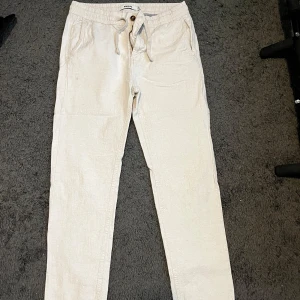 Beige linnebyxor från Kappahl W31 L32 - Snygga beige linnebyxor från Kappahl med avslappnad passform och dragsko i midjan. Byxorna har fickor på sidorna och knappstängning framtill. Perfekta för chill dagar och sommarhäng, riktigt sköna och luftiga.