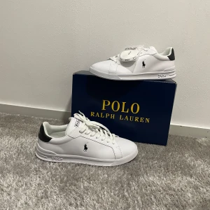 Polo Ralph Lauren skor - Fräscha vita sneakers från Polo Ralph Lauren med svart detalj på hälen och klassisk Polo-logga på sidan. Skorna har snörning, rund tå och platt sula. Materialet är syntet med en mjuk innersula för extra komfort. Perfekt för dig som gillar stilrena och cleana sneakers. Helt sprillans nya ur paket och oanvända. Nypris 1599kr. Säljer för endast 999kr😊