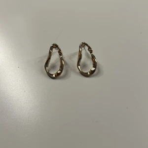  guldörhängen i metall - Unika örhängen i guldtonad metall med organisk, vågig form. Perfekta för dig som gillar statement-smycken med modern vibe. De har en cool, oregelbunden design som verkligen sticker ut och passar till alla tillfällen när du vill glänsa lite extra.