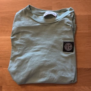 Mintgrön Stone Island t-shirt - Mintgrön t-shirt från Stone Island. T-shirten har en snygg svart patch med logga på bröstet och är gjord i mjuk bomull. Passar till nästan allt och är otroligt skön att ha på sig. T-shirten sitter ca 150-160cm. 160 kan kännas tajt dock.