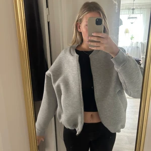 Grå bomberjacka från Gina Tricot - Säljer en grå bomberjacka från Gina Tricot i storlek M. Jackan har en loose passform, ribbad krage och muddar, samt dragkedja framtill. Materialet är mjukt och känns som syntet. Perfekt för dig som gillar en chill och stilren look.