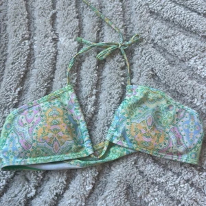 Pastellfärgad bikiniöverdel med snörning - Snygg bikiniöverdel i pastellfärger med paisley-inspirerat mönster i ljusgrön, gul, rosa och blå. Modellen har trekantsform och knyt både i nacken och ryggen för perfekt passform. Perfekt för strandhäng och poolparty! Man kan även ha den lite hur man vill ha den på.