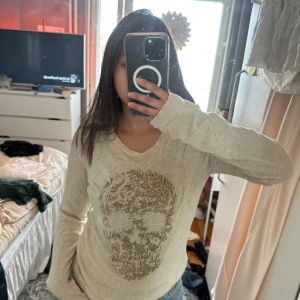 Beige tröja med döskalle från Zadig & Voltaire - Snygg beige långärmad tröja från Zadig & Voltaire med ett stort döskallemotiv i guldiga paljetter på framsidan. Tröjan har rund hals och är gjord i mjuk bomull.
