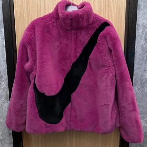 Nike teddyjacka i mörkrosa S - Nike teddyjacka i mörkrosa. Jackan har hög krage och är tillverkad i mjuk polyester som ger en fluffig och cozy känsla. Perfekt för dig som vill sticka ut med en bold look och älskar streetwear.