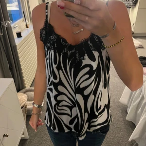 Svartvit linnetopp från Amisu XS - Snygg linnetopp från Amisu i svartvitt abstrakt mönster. Toppen har tunna axelband och spetsdetaljer vid urringningen som ger en extra touch. Perfekt att styla med jeans eller kjol för en cool look.