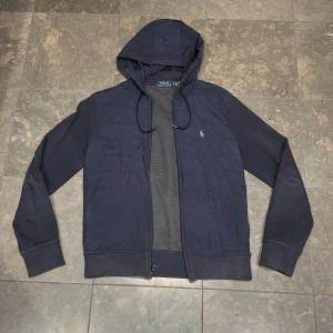 Polo Ralph Lauren cardigan  - Mörkblå hoodiejacka från Polo Ralph Lauren med quiltad front, broderad logga på bröstet och dragkedja. Jackan har huva med snörning och mjuka ärmar i bomullsmix. Perfekt för lager-på-lager och chill stil. skick 7-10