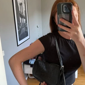 Svart axelväska i crocomönster - Svart handväska i crocomönster från Nelly. Har dragkedja. Använd några gånger.