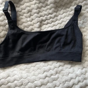 Svart bh/topp Gina Tricot  - Toppen har en enkel och clean design med bred resår nedtill för extra komfort. Materialet är mjukt och stretchigt, vilket gör den skön att bära hela dagen.
