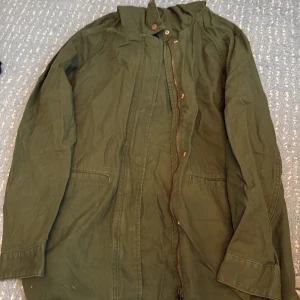 Grön parkajacka från L.O.G.G. - Säljer en snygg grön parkajacka från L.O.G.G. i storlek 36. Jackan har huva med snörning, dragkedja och knappar framtill samt två fickor. Perfekt för dig som gillar en chill och urban stil. Materialet är bomull och jackan har en loose passform.