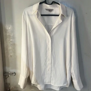 Vit klassisk skjorta från H&M - Snygg vit skjorta från H&M i klassisk modell med krage och knappar framtill. Långärmad med breda manschetter och rak passform. Perfekt att styla med jeans eller kostymbyxor för en clean look.