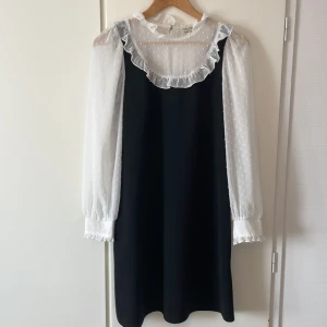 Svartvit kort klänning med volangkrage från Miss selfridge - Svart klänning med vita, transparenta långärmar och volangkrage. Ärmarna har diskret prickigt mönster och avslutas med volangdetalj vid manschetten. Klänningen har en klassisk, rak passform. Strl 38 men passar även 36. Använt max 2 gånger och är fortfarande i väldigt bra skick.