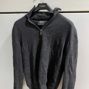 Svart merinoullströja från Hugo Boss - Snygg mörkgrå långärmad tröja från Hugo Boss i 100% extra fin merinoull. Tröjan har en hög krage med half zip-dragkedja och en klassisk, stilren look. Perfekt för dig som gillar en clean och tidlös stil. Priser kan diskuteras!!
