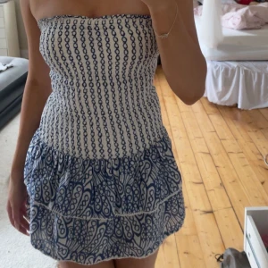 Vit och blå tubklänning Gina Tricot - Supersöt kort tubklänning från Gina Tricot i vitt och blått. Klänningen har smockad överdel och volangig kjol med blått mönster.