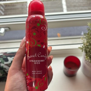 Sweet Candy Strawberry Kiss Body Spray - Söt body spray för kvinnor med jordgubbsdoft från Sweet Candy. Flaskan är röd med gröna och vita detaljer samt text i vitt. Innehåller 150 ml och har en rundad form med röd plastkork. Perfekt för dig som gillar fruktiga och lekfulla dofter.