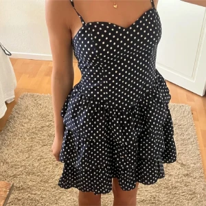 Mörkblå prickig kortklänning - Supersöt mörkblå kortklänning med vita prickar och volangkjol. Klänningen har hjärtformad urringning och kan bäras både med smala axelband eller axelbandslös. Perfekt för dig som gillar en lekfull och trendig stil.