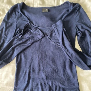 Mörkblå långärmad topp Gina Tricot - Mörkblå långärmad topp från Gina Tricot i stretchig bomullsmix. Snygg, enkel design med rund halsringning och figurnära passform. Perfekt att styla med jeans eller kjol för en clean look. Tröjan har ett liten hål vid ena armen och måste rollas för den har hängt på en galje ett bra tag!