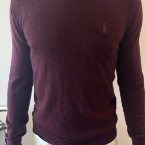 Vinröd merinoullströja Polo Ralph Lauren - Säljer en vinröd långärmad tröja från Polo Ralph Lauren i merinoull. Lite sömnproblem längst ner, kolla bilden vid midjan 