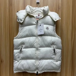 Vit dunväst från Moncler - Snygg och puffig vit dunväst från Moncler med hög krage och två dragkedjefickor framtill. Västen har en klassisk quiltad design och stängs med dragkedja. Perfekt för lager-på-lager och har Moncler-logga på bröstet.