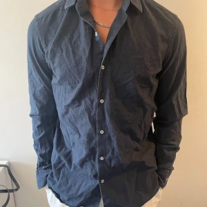 Mörkblå skjorta från Massimo Dutti - Stilren mörkblå skjorta från Massimo Dutti med klassisk krage och vita knappar. Skjortan är långärmad och har en normal passform, perfekt för dig som gillar en enkel men snygg look. Tillverkad i mjuk bomull som känns skön mot huden.