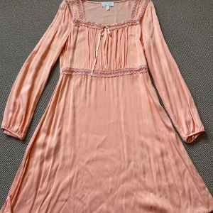 Ljusrosa klänning från & Other Stories str 38 - Använd två gånger! Superfin ljusrosa kortklänning från & Other Stories Los Angeles Atelier. Klänningen har långa ärmar, spetsdetaljer och söt knytning framtill. Tillverkad i ett glansigt, mjukt material som ger en lyxig känsla. Perfekt för dig som gillar romantiska vibes.