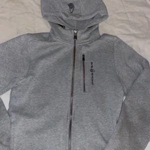 Grå hoodiejacka från Sail Racing - Grå hoodiejacka från Sail Racing med dragkedja framtill och en extra bröstficka med dragkedja. Även innerfickor. Storlek 170. Pris kan diskuteras vid snabbt köp!